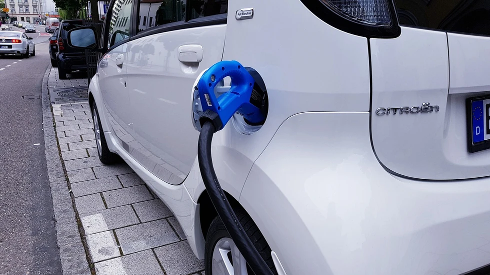 A white electric car charging at the roadside with a blue plug